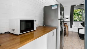 Een compact keukenhoekje met een magnetron, een koelkast en een klein zitehoek met een stoel en tafel.
