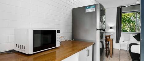 Una kitchenette compacta con microondas, un refrigerador y un pequeño comedor con una silla y mesa.