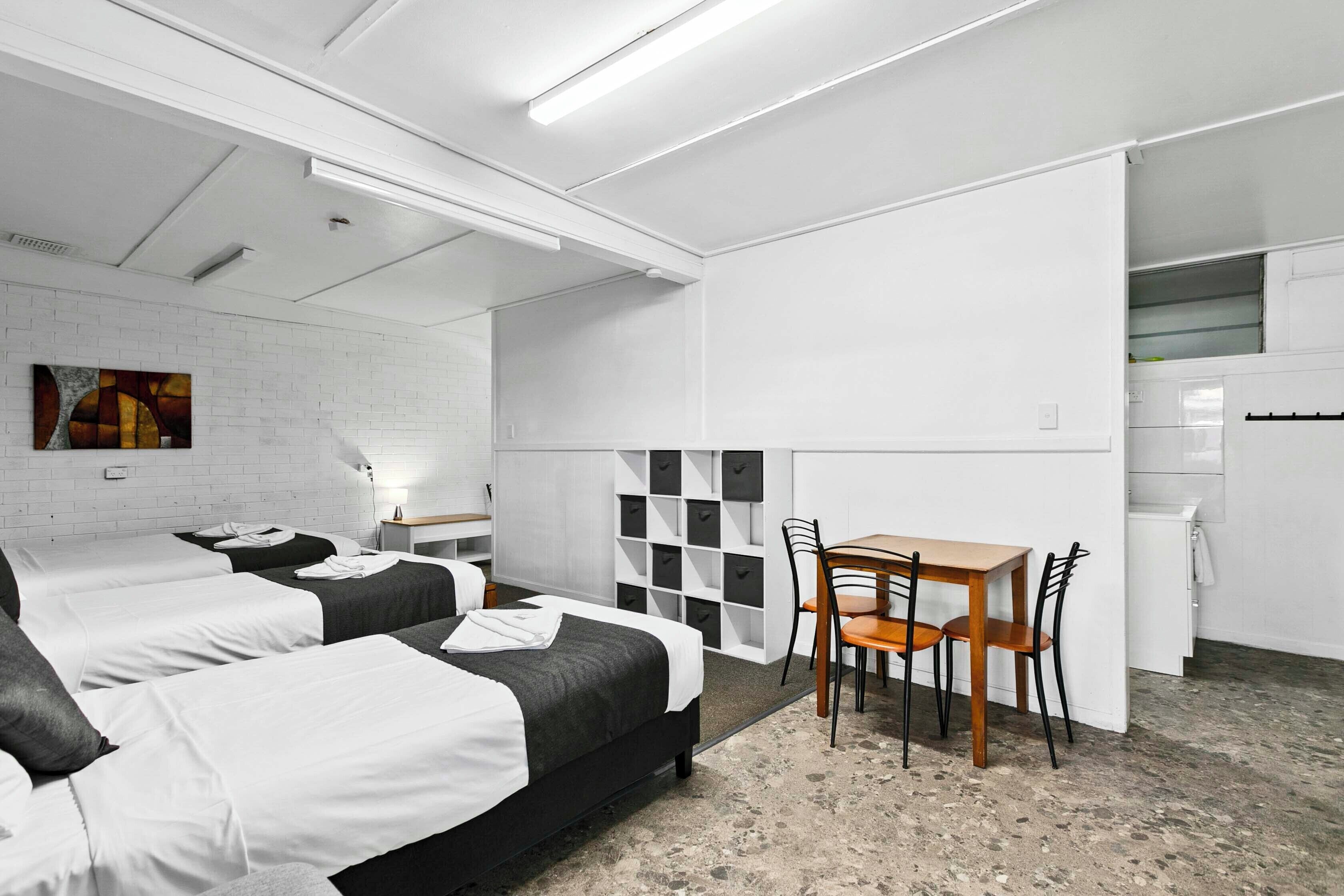 Moderni hotellihuone, jossa on kaksi sänkyä, ruokapöytä ja pieni keittiönurkkaus.