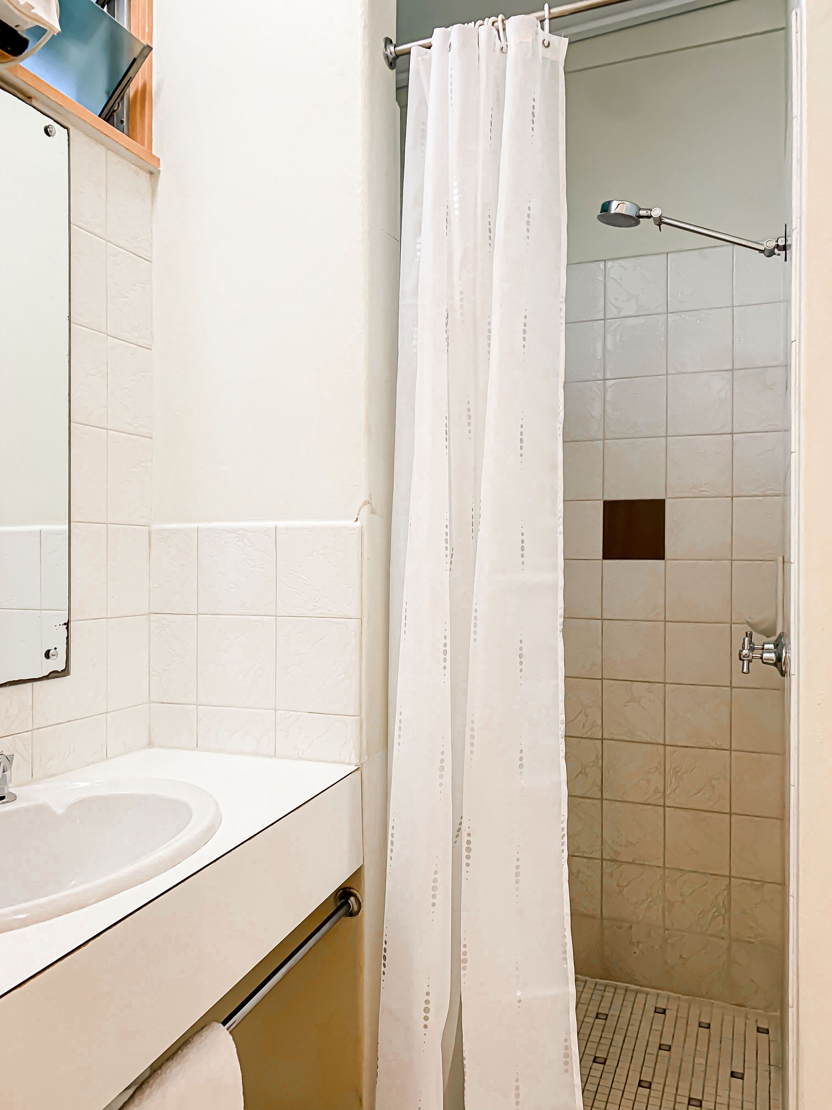 A bathroom with a white sink, a mirror, and a shower area with a white curtain.