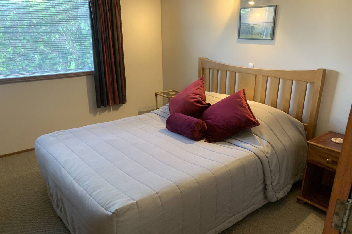 A neatly made bed with a wooden headboard, two pillows, a bedside table, and a framed picture on the wall.