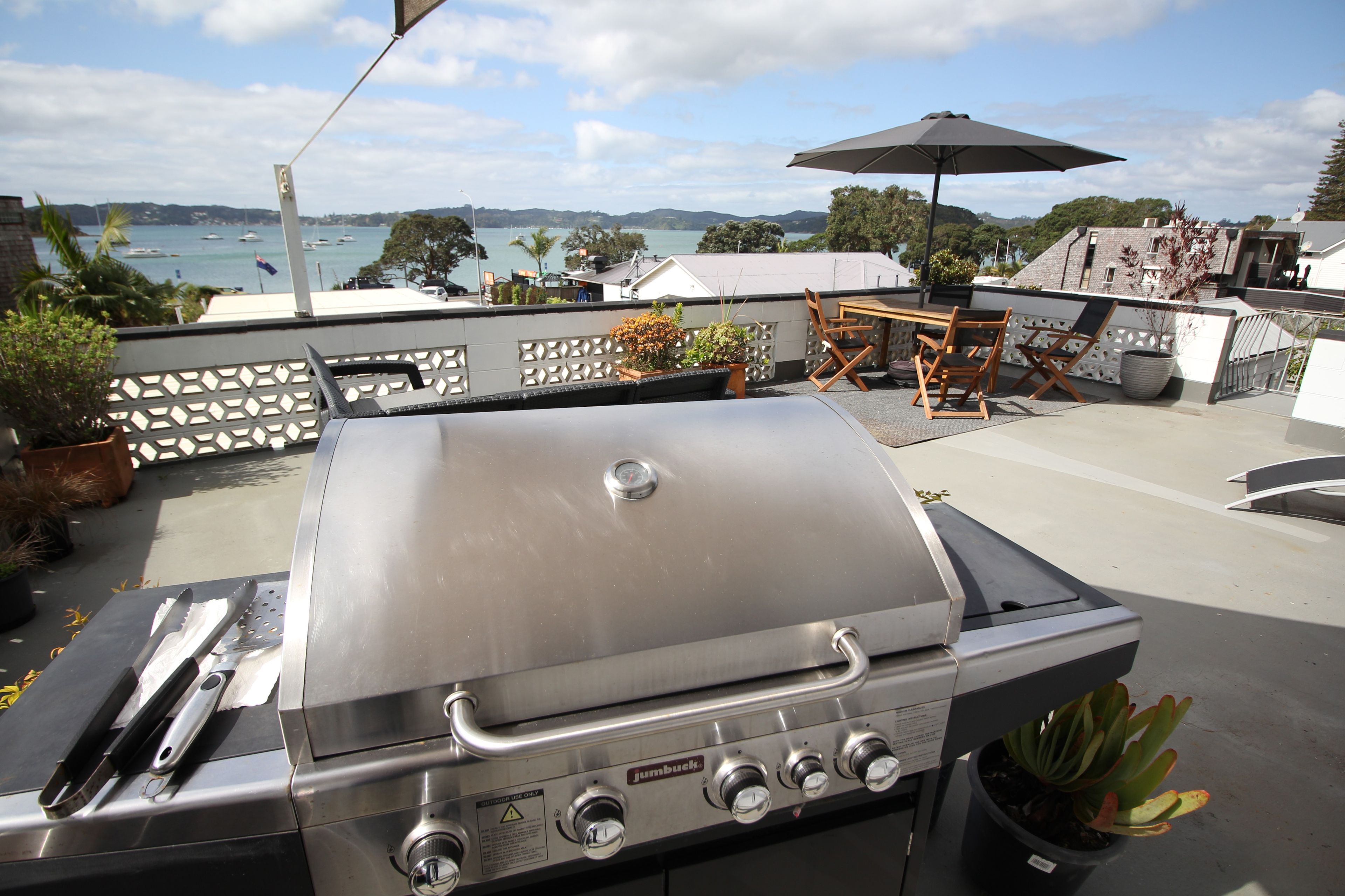 Un barbecue extérieur avec commandes, une table et des chaises, et une vue sur la mer et les collines en arrière-plan.