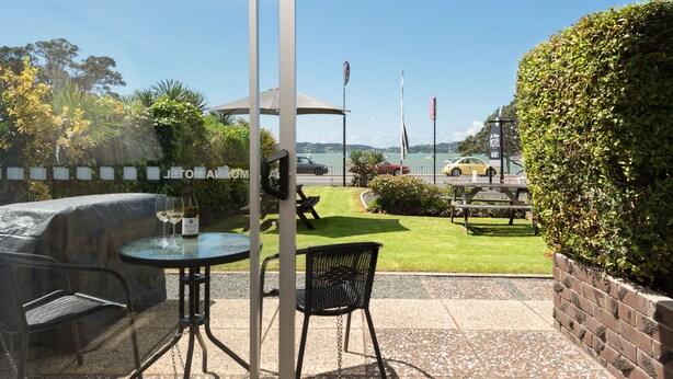 An outdoor patio with a grill, seating, and a view of the sea. - Ala Moana Motel (Paihia)