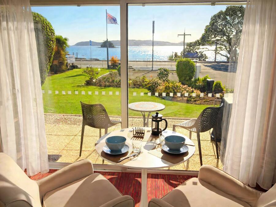 Quarto com vista para um jardim paisagístico e o mar. Há uma mesa com cadeiras e uma cafeteira.