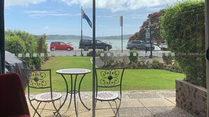 A patio with two tables and chairs, a flag, and a view of the sea and parked cars. - Ala Moana Motel (Paihia)
