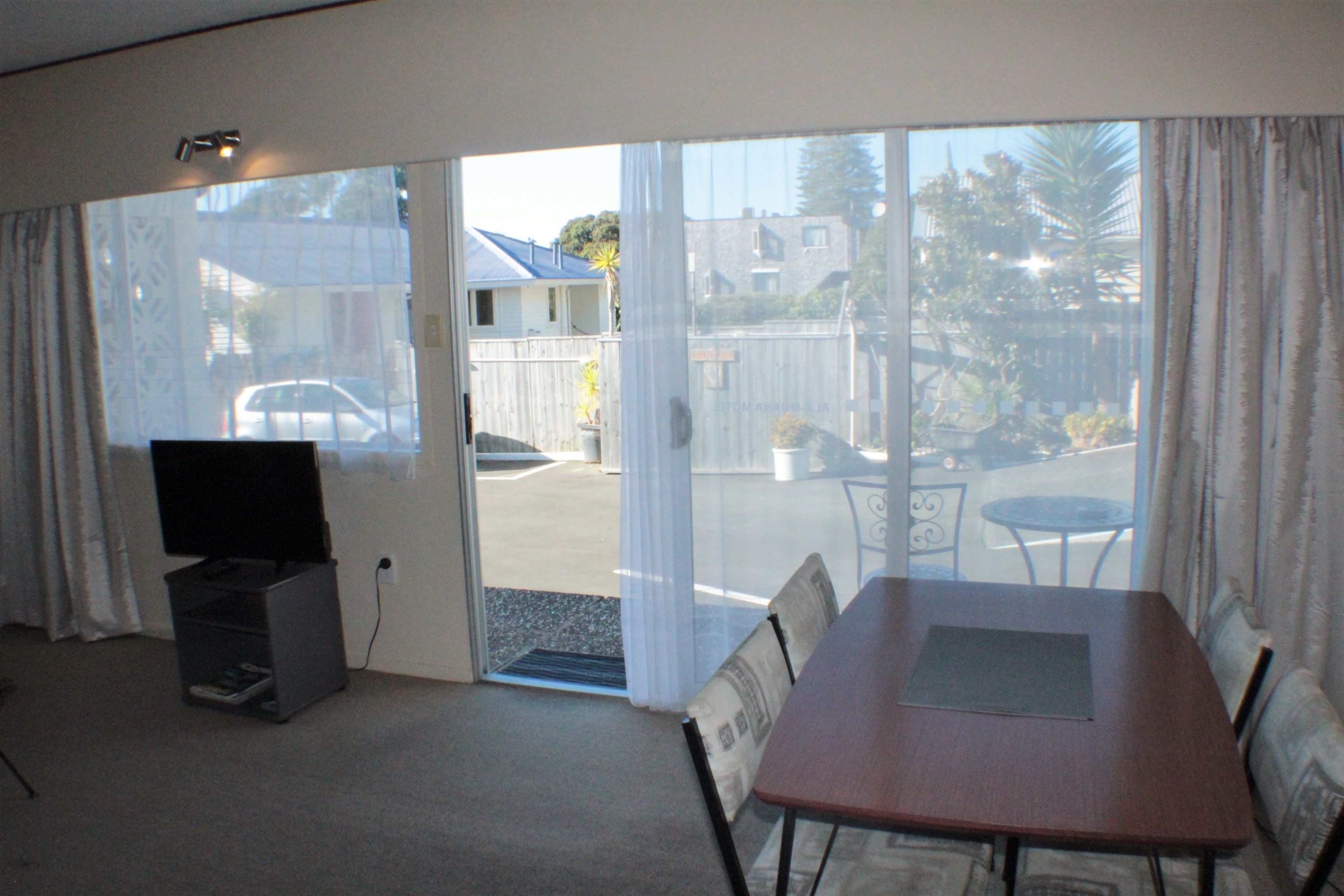 Una habitación con puerta de cristal corredera que da a un balcón, un mueble para televisión, una mesa de comedor y una silla.