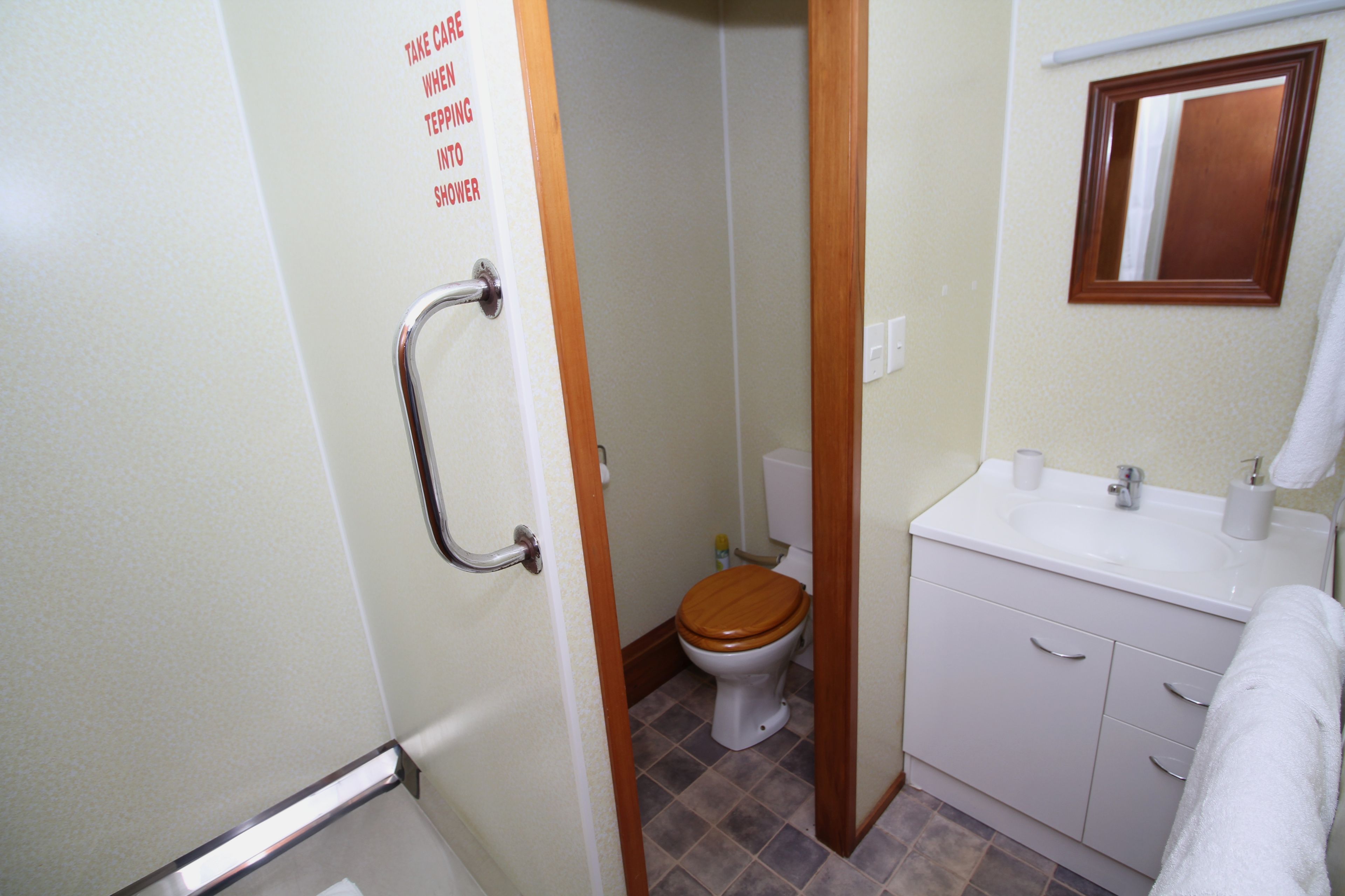A bathroom with a wooden toilet, a white sink, and a handrail.