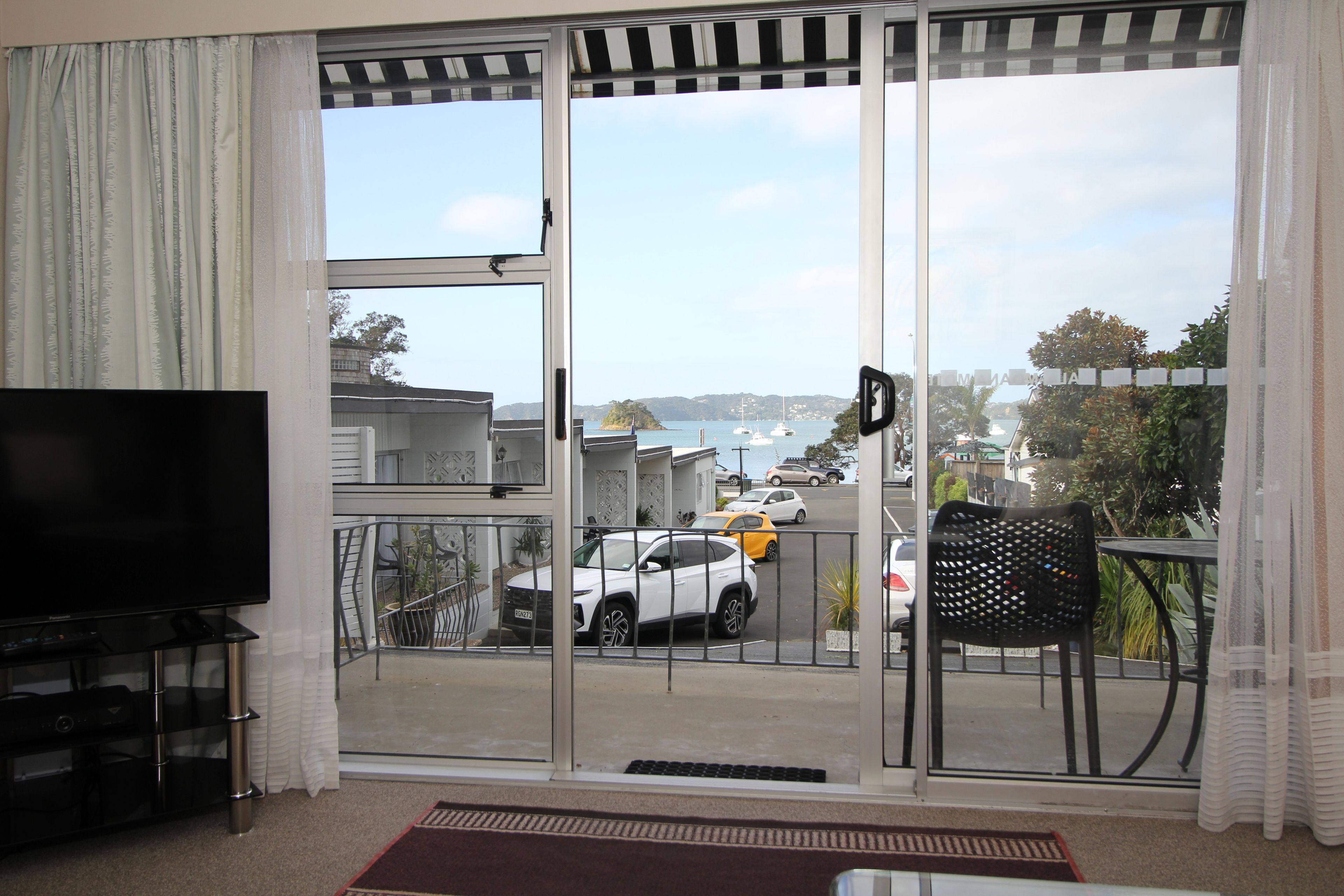 A room with a sliding glass door leading to a balcony with a view of parked cars and boats.