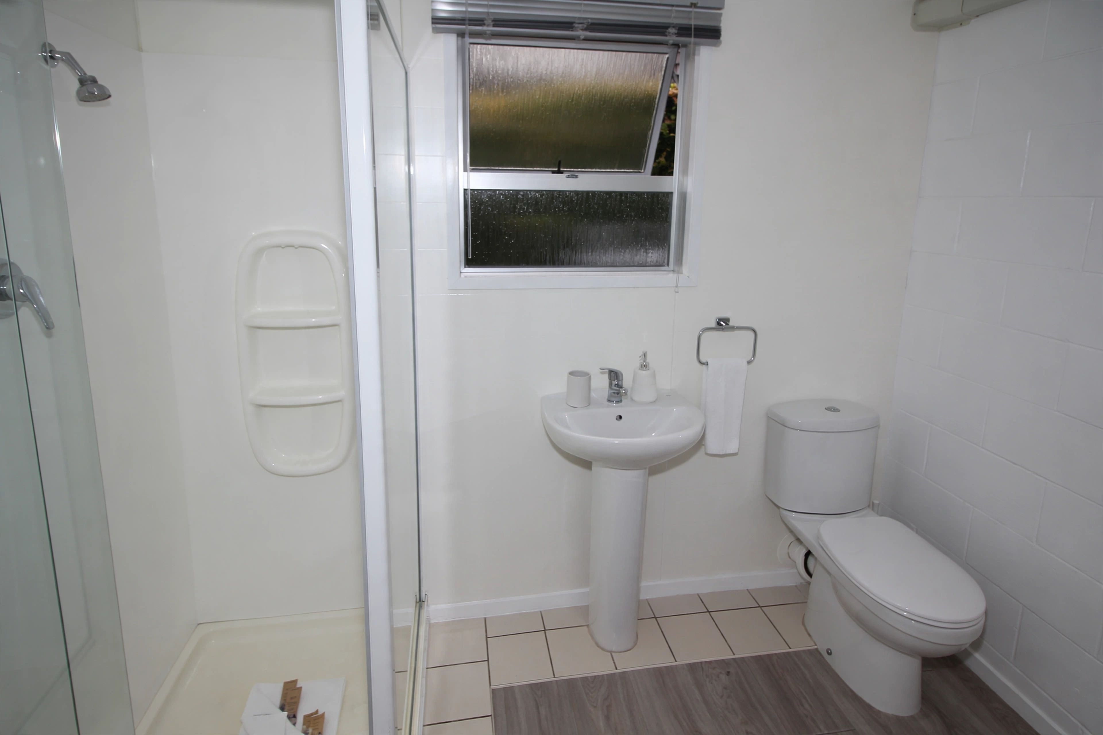 A bathroom with a shower, sink, toilet, and a window.