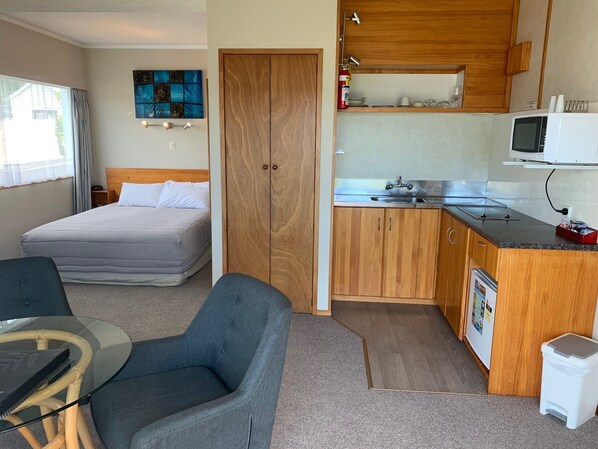 Habitación de hotel compacta con cama, kitchenette, comedor y baño.