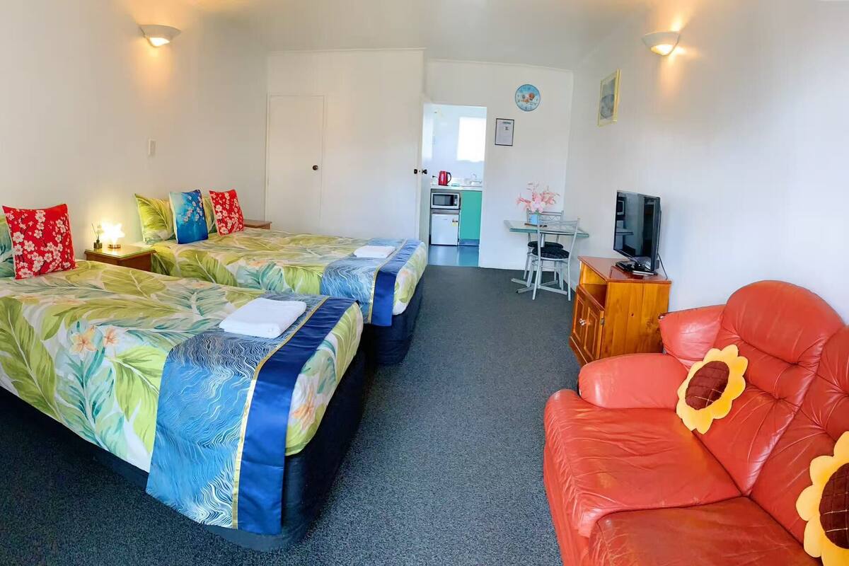 A hotel room with two beds, a red sofa, a TV, and a kitchenette in the background.