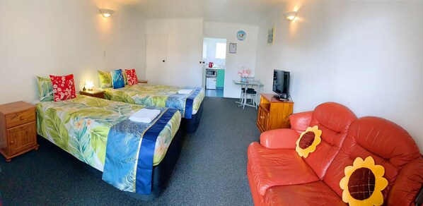 A hotel room with two beds, a red sofa, a TV, and a kitchenette in the background.