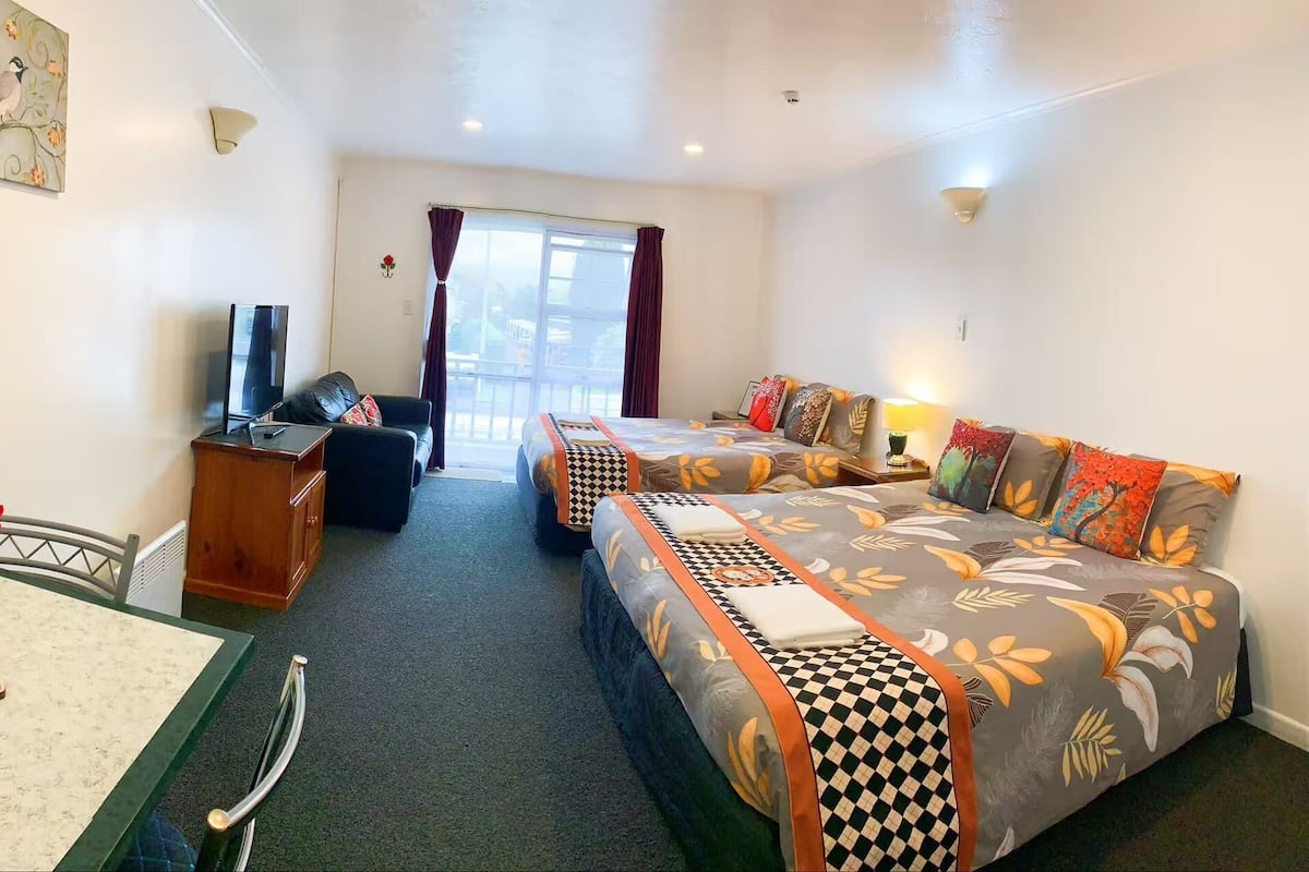 A hotel room with two beds, a desk, a chair, a TV, and a window with curtains.
