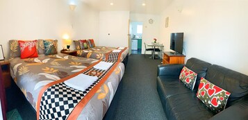 Een hotelkamer met twee bedden, een bank, een televisie en een kitchenette.