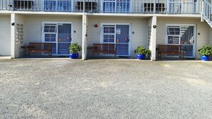 A two-story motel with three doors, each with a number. There are benches and potted plants in front of the doors. - Kerry's Motel (Rotorua)