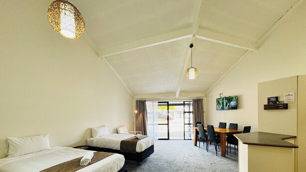 A hotel room with two beds, a desk, and a view through a glass door.