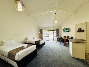Quarto de hotel com duas camas, uma escrivaninha e vista através de uma porta de vidro.