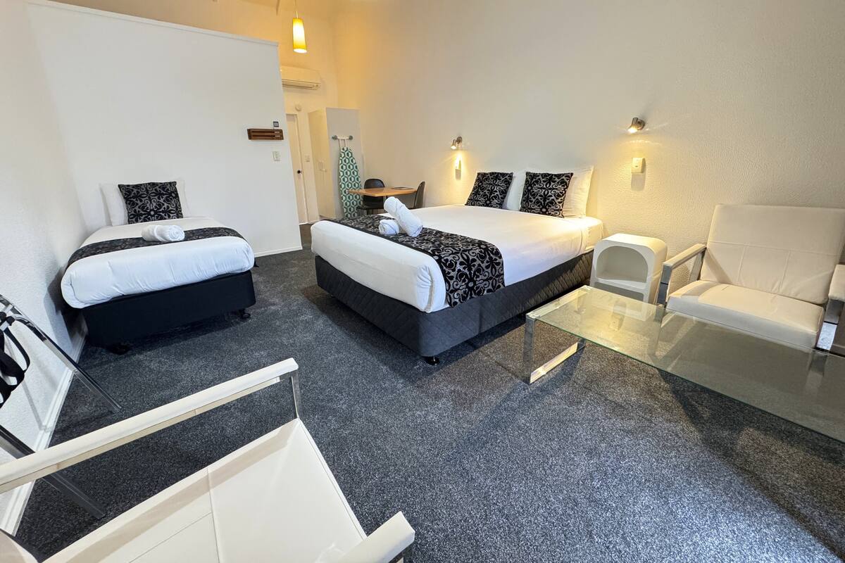 Une chambre d’hôtel avec deux lits, une table en verre, un fauteuil blanc et un petit bureau avec une chaise.