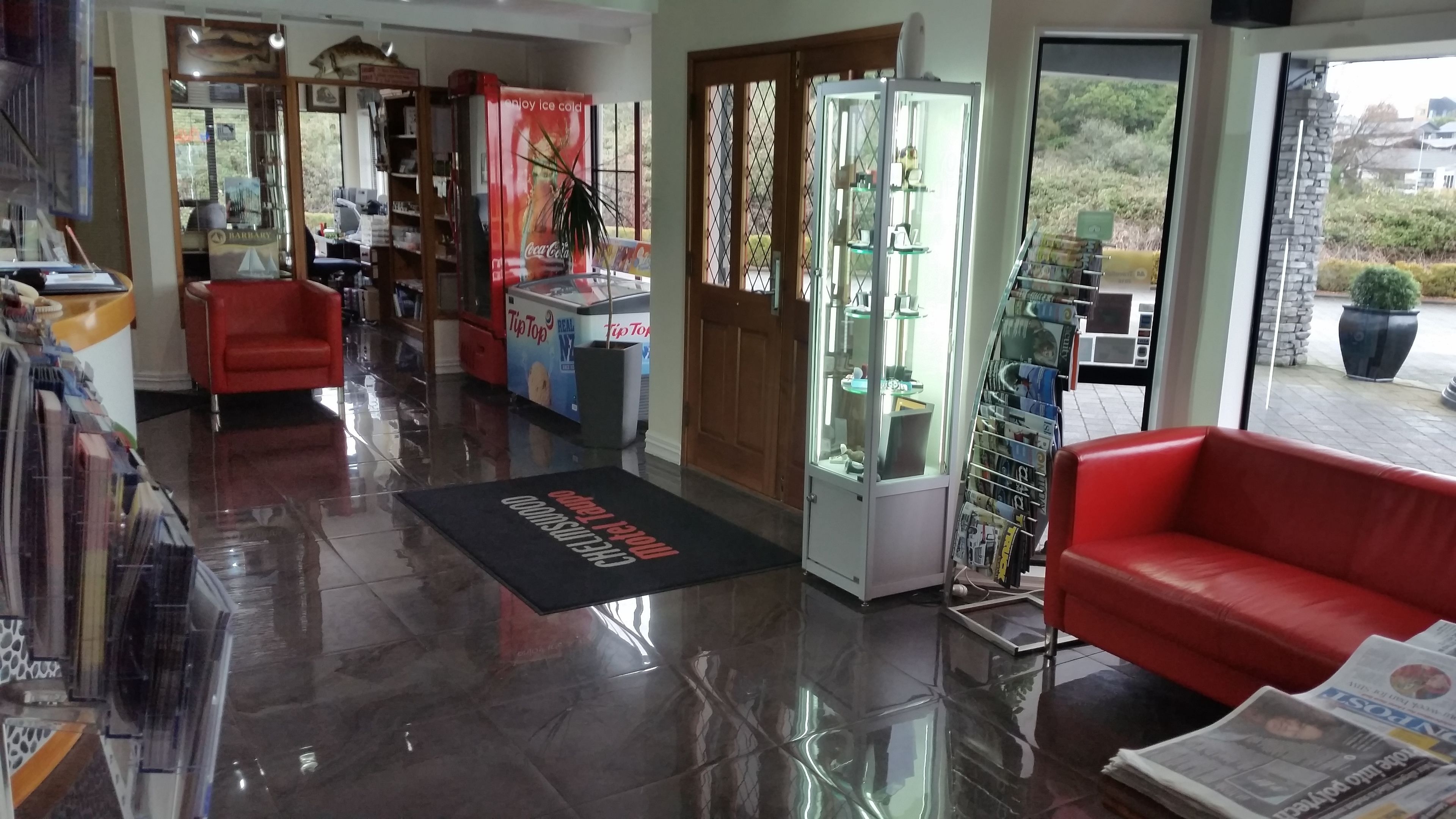 Um hall de hotel com um sofá vermelho, um refrigerador de Coca-Cola e uma vitrine de vidro.
