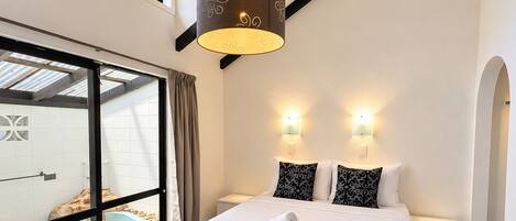 Una habitación de hotel con una cama grande, dos lámparas de noche, un ventanal con vistas a una piscina y un candelabro.