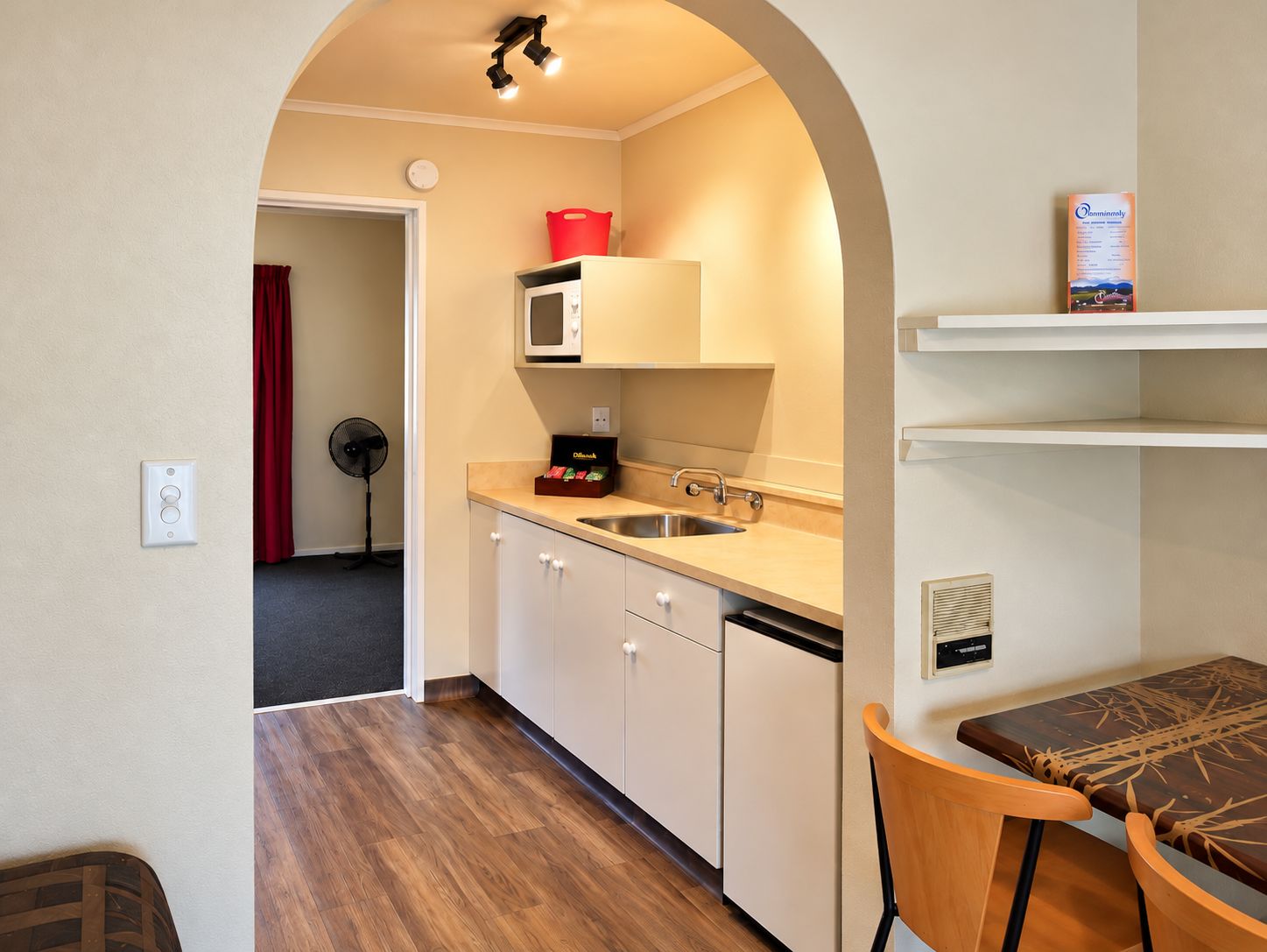 A compact kitchen with a microwave, sink, and a red basket on the countertop.