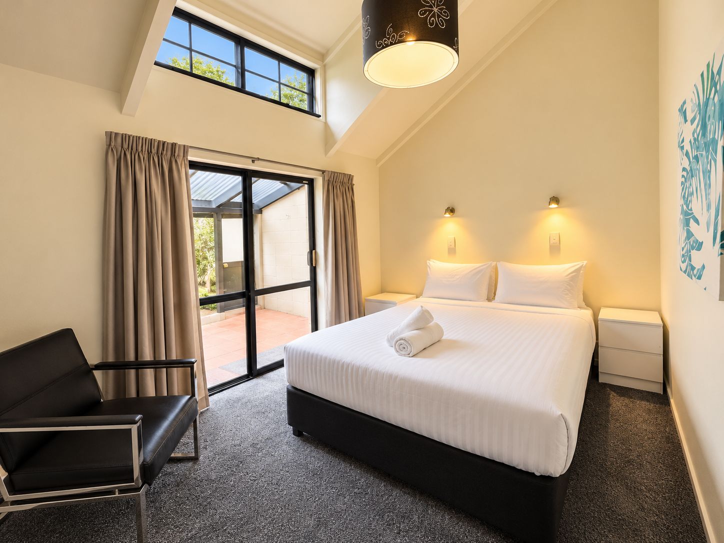 A hotel room with a bed, a chair, a desk, a lamp, and a view of the outdoors.