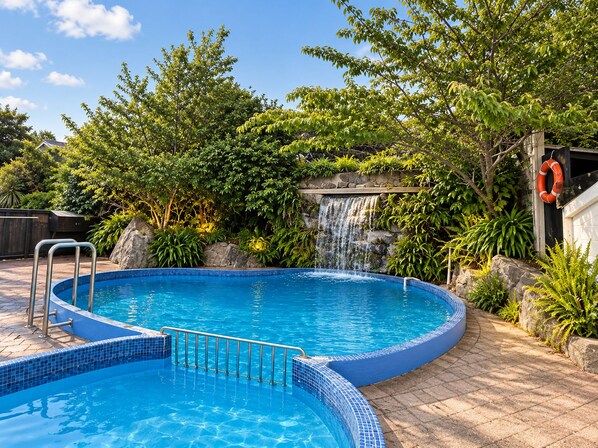 A swimming pool with a waterfall feature, surrounded by lush greenery and a lifebuoy.