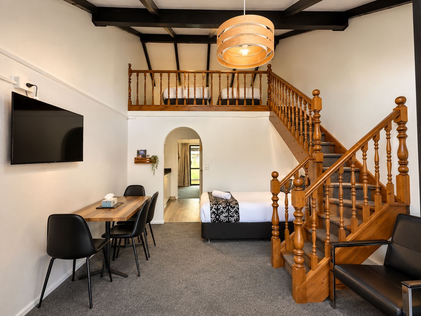 A room with a dining table, chairs, a TV, a staircase, and a bed.