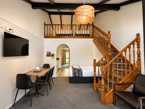 Une pièce comprenant une table à manger, des chaises, un téléviseur, un escalier et un lit.