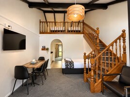 Una habitación con una mesa de comedor, sillas, un televisor, una escalera y una cama.