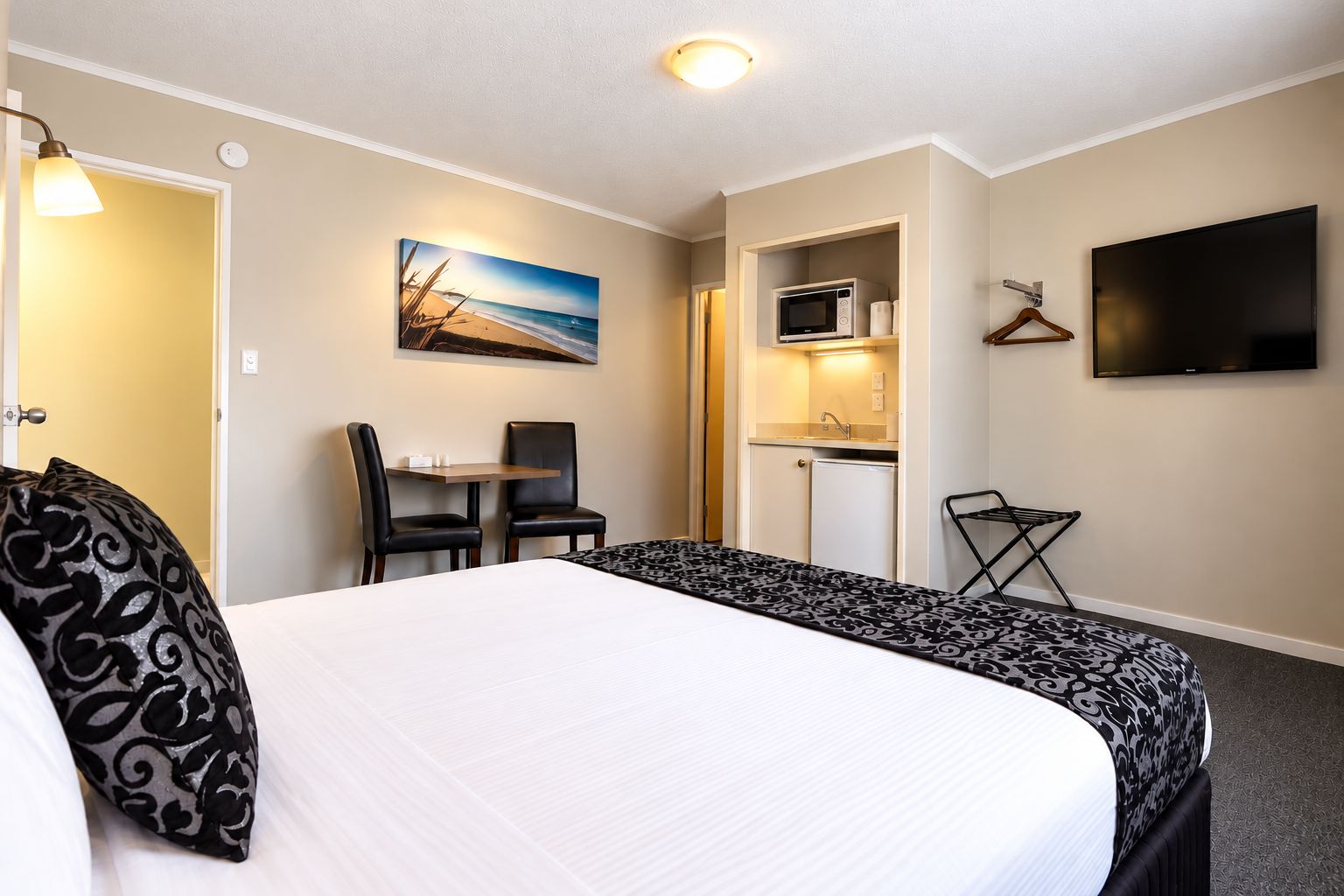 Quarto de hotel com uma cama grande, uma escrivaninha com duas cadeiras, micro-ondas, televisão e um quadro na parede.