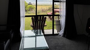 A room with a glass table, two chairs, a view of a landscape through large windows, and a ceiling light.