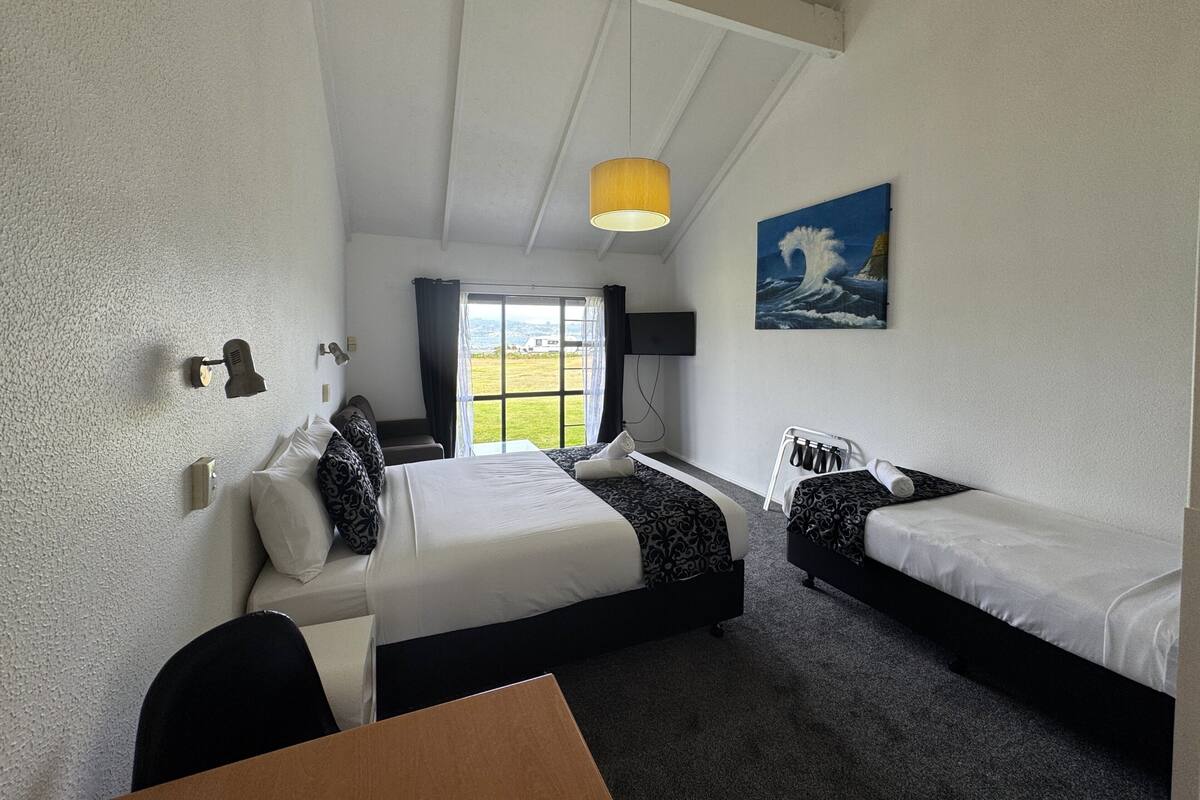 Une chambre d’hôtel avec deux lits, un bureau, une chaise, une télévision et un tableau au mur.