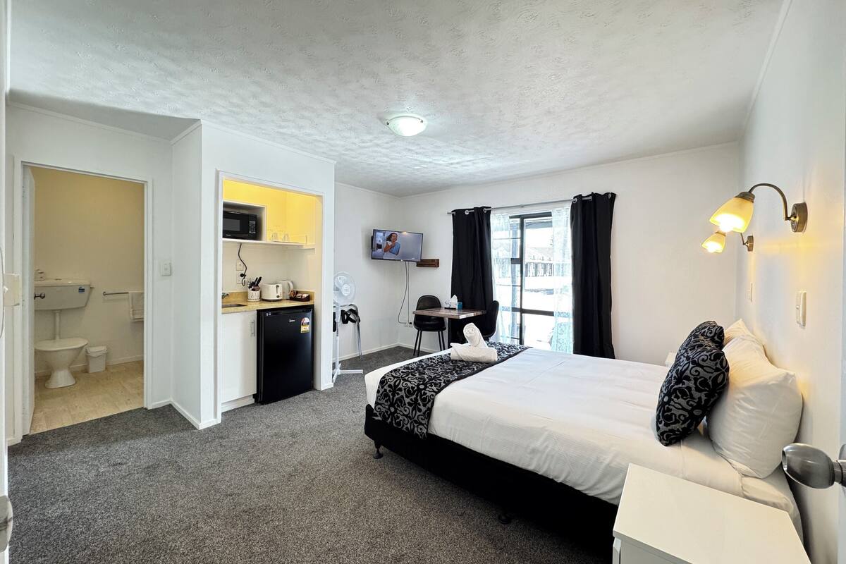 Une chambre d’hôtel équipée d’un lit, d’un bureau, d’une chaise, d’une télévision et d’une kitchenette.