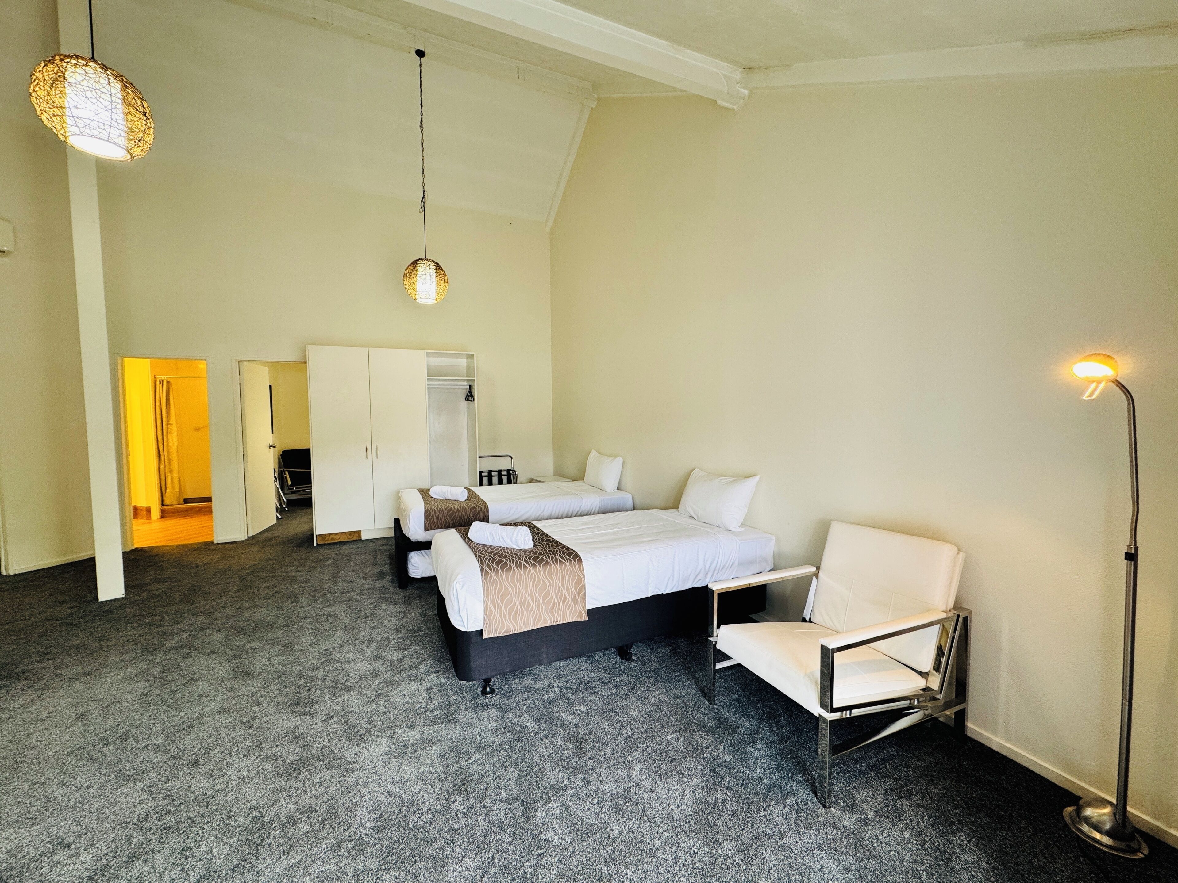 Een hotelkamer met twee bedden, een kledingkast, een stoel en een vloerlamp.