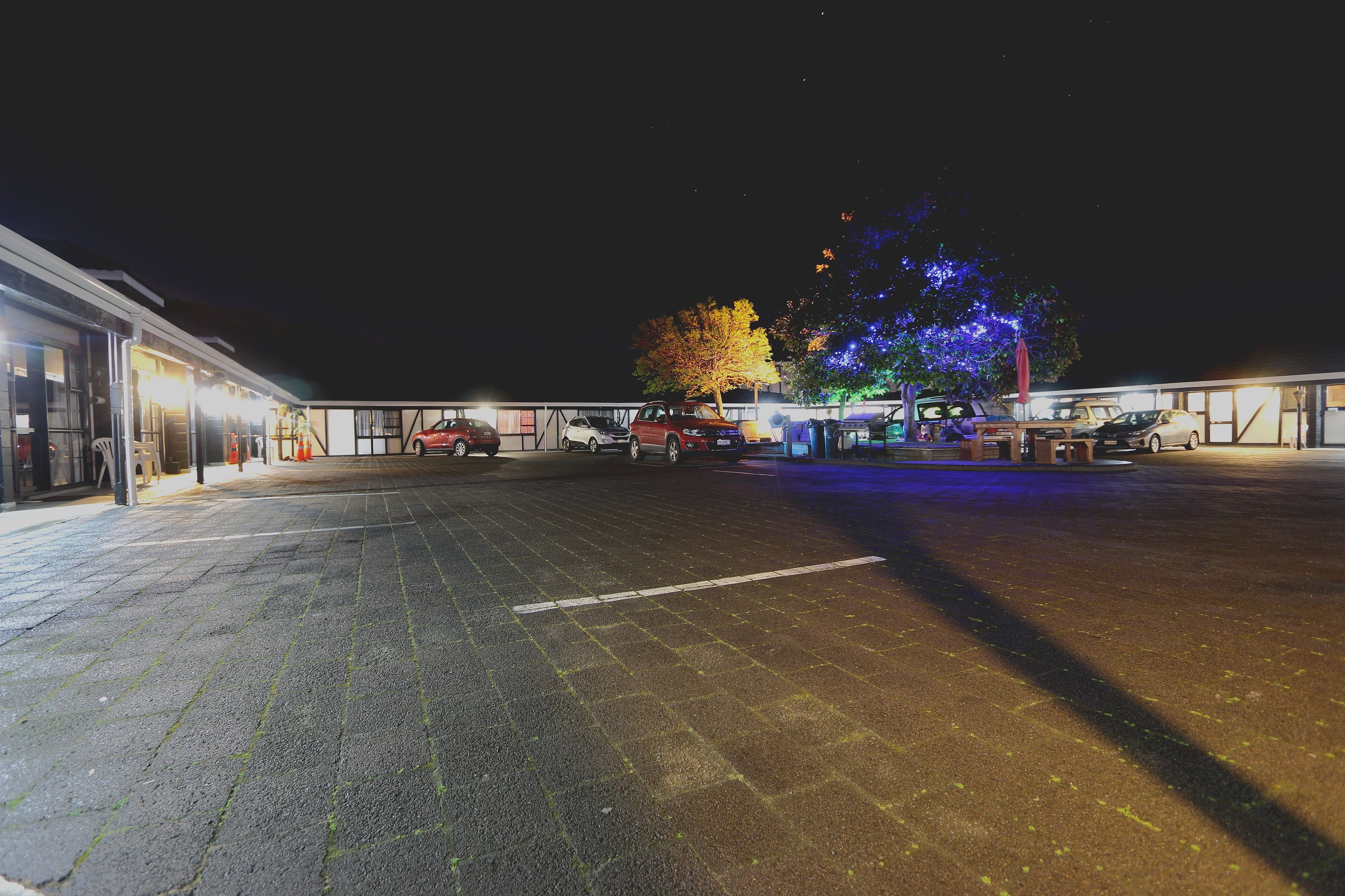 A parking lot with several cars and a building with illuminated windows.