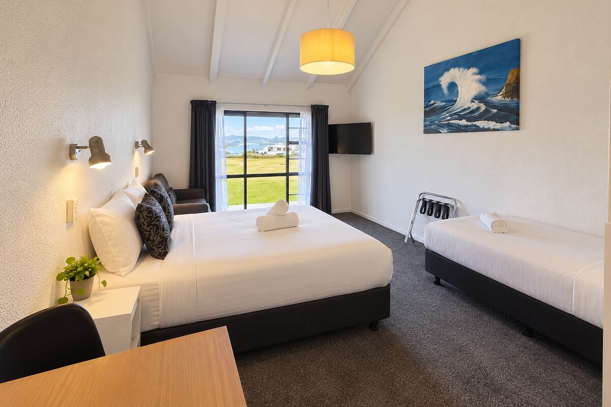 A hotel room with a bed, bedside table, lamp, TV, and a painting of a wave.