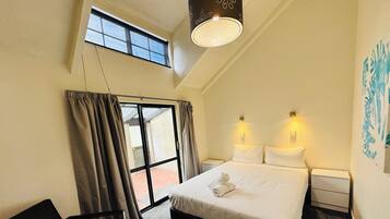 Una camera d'hotel con un letto, due lampade da comodino, una sedia, una finestra con tende e un lampadario.