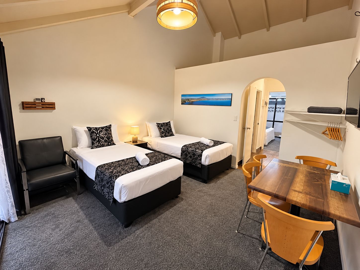 A hotel room with two beds, a desk, a chair, a lamp, and a painting on the wall.