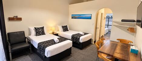 A hotel room with two beds, a desk, a chair, a lamp, and a painting on the wall.