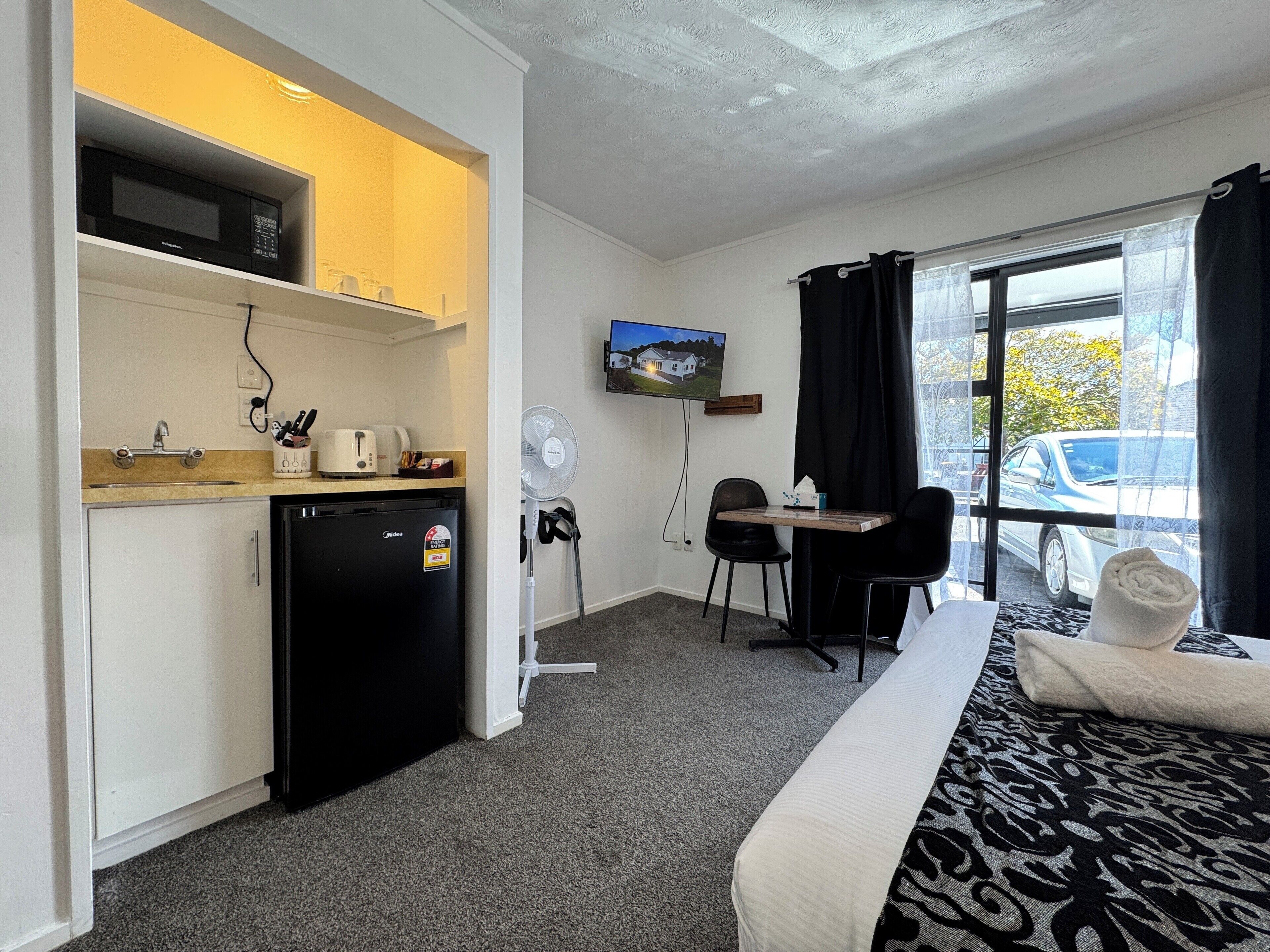 Habitación de hotel con cama, escritorio, kitchenette, televisor y vistas al exterior.
