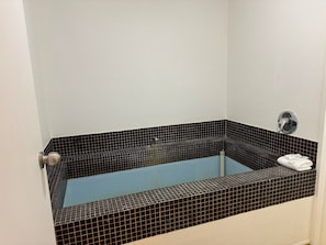 A bathtub with black and white mosaic tiles, a white towel on the edge, and a silver faucet.