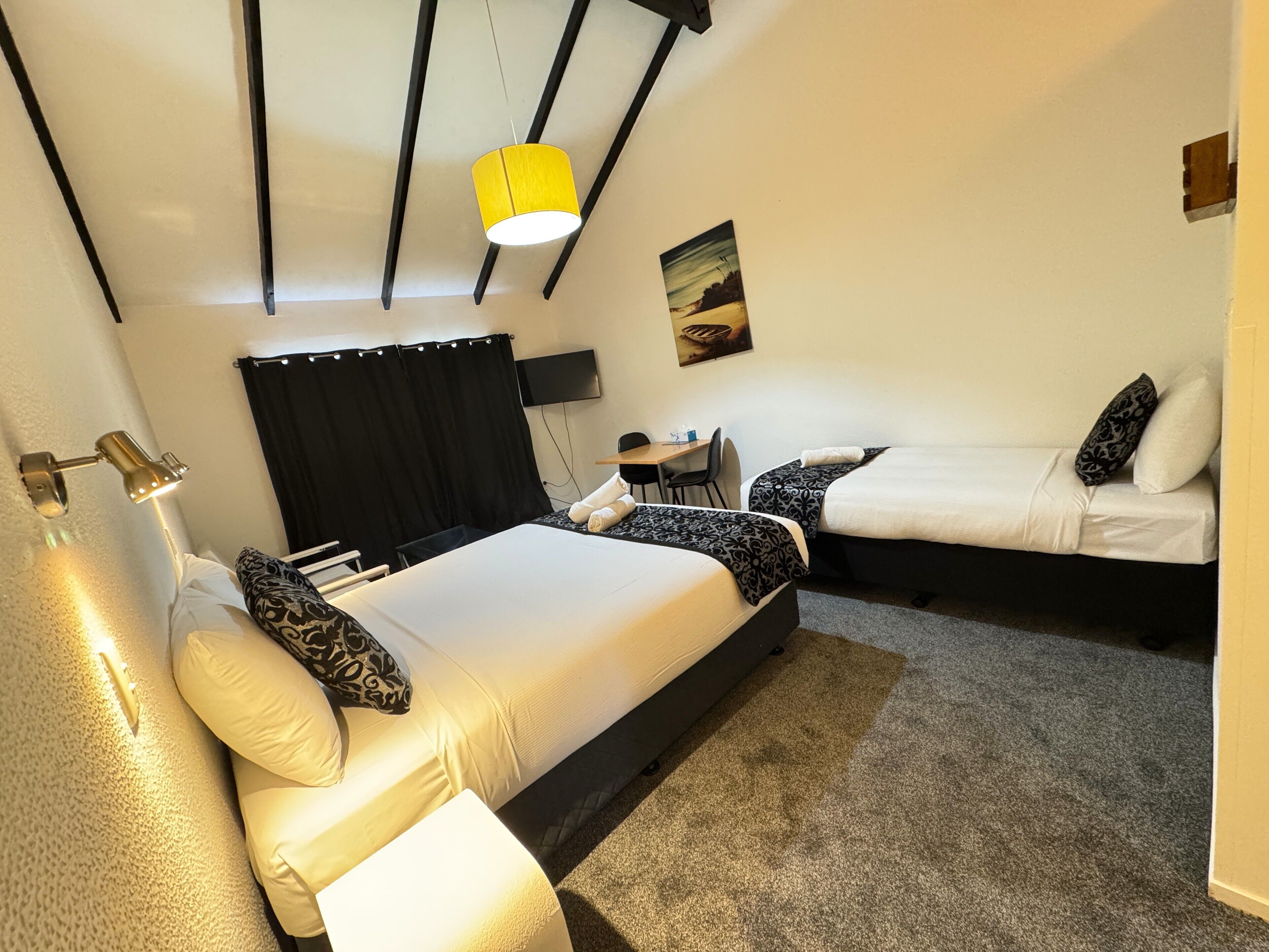A hotel room with two beds, a desk, a chair, a flat-screen TV, and a painting on the wall.