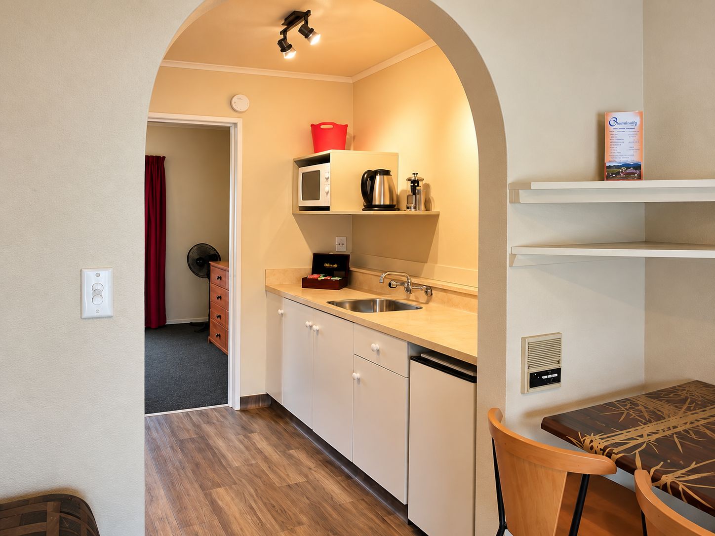 Eine kleine Küche mit Mikrowelle, Spüle und einem Kühlschrank. Ein Holztisch mit Stühlen steht bereit.