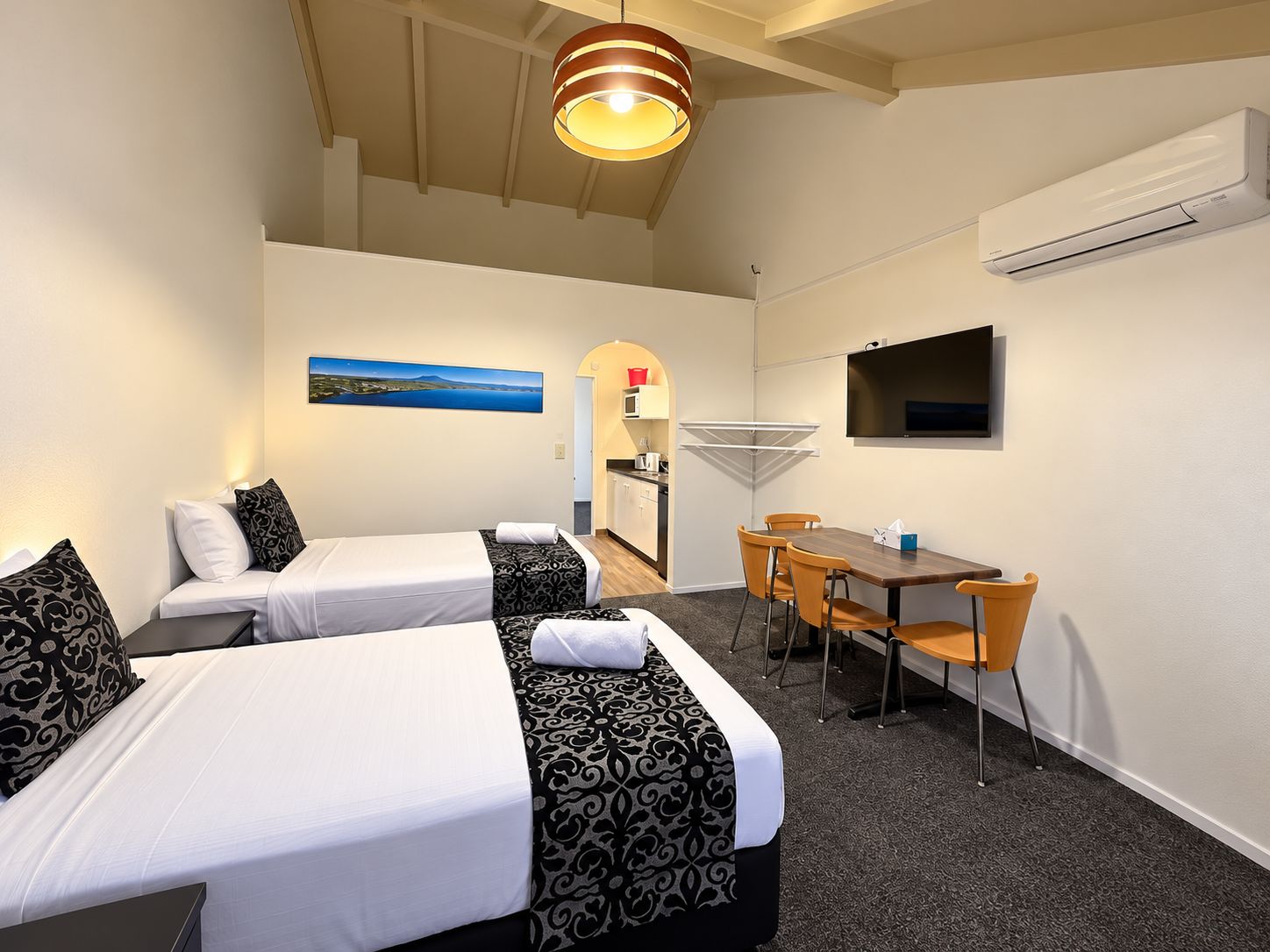Habitación de hotel con dos camas, una mesa de comedor, un televisor y un equipo de aire acondicionado.