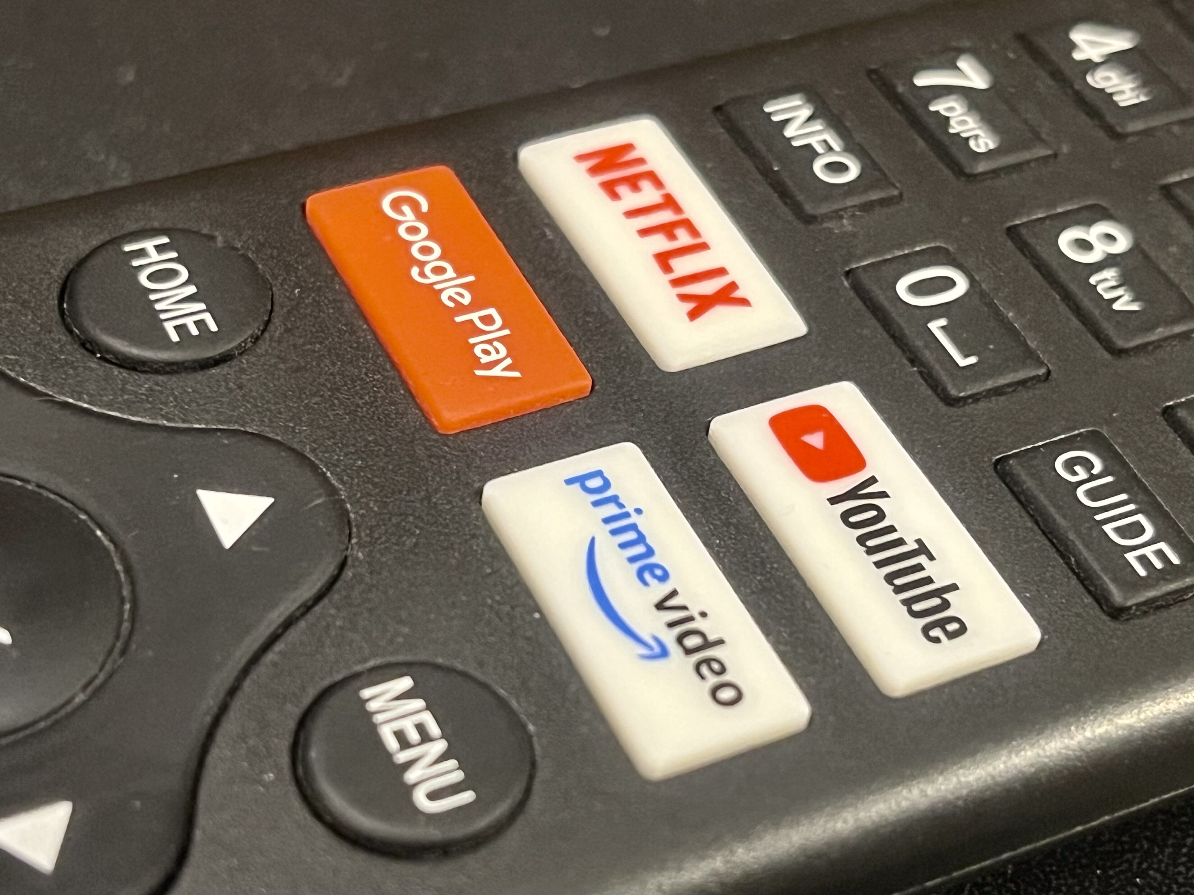 Primer plano de un control remoto con botones etiquetados HOME, GOOGLE PLAY, NETFLIX, PRIME VIDEO e YOUTUBE.