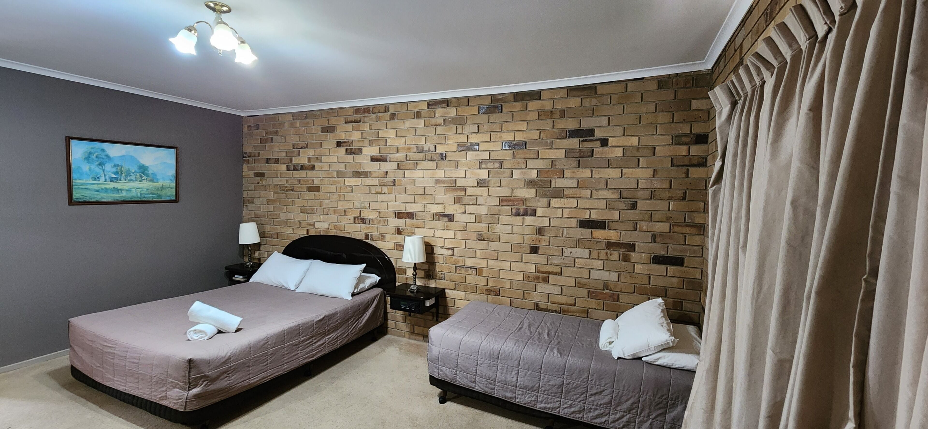 Habitación de hotel con dos camas, pared de ladrillo, un cuadro y una lámpara en el techo.