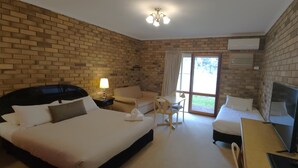 A hotel room with a brick wall, a large bed, a desk with a chair, a sofa, and a TV. - Magdala Motor Lodge & Lakeside Restaurant (Stawell)
