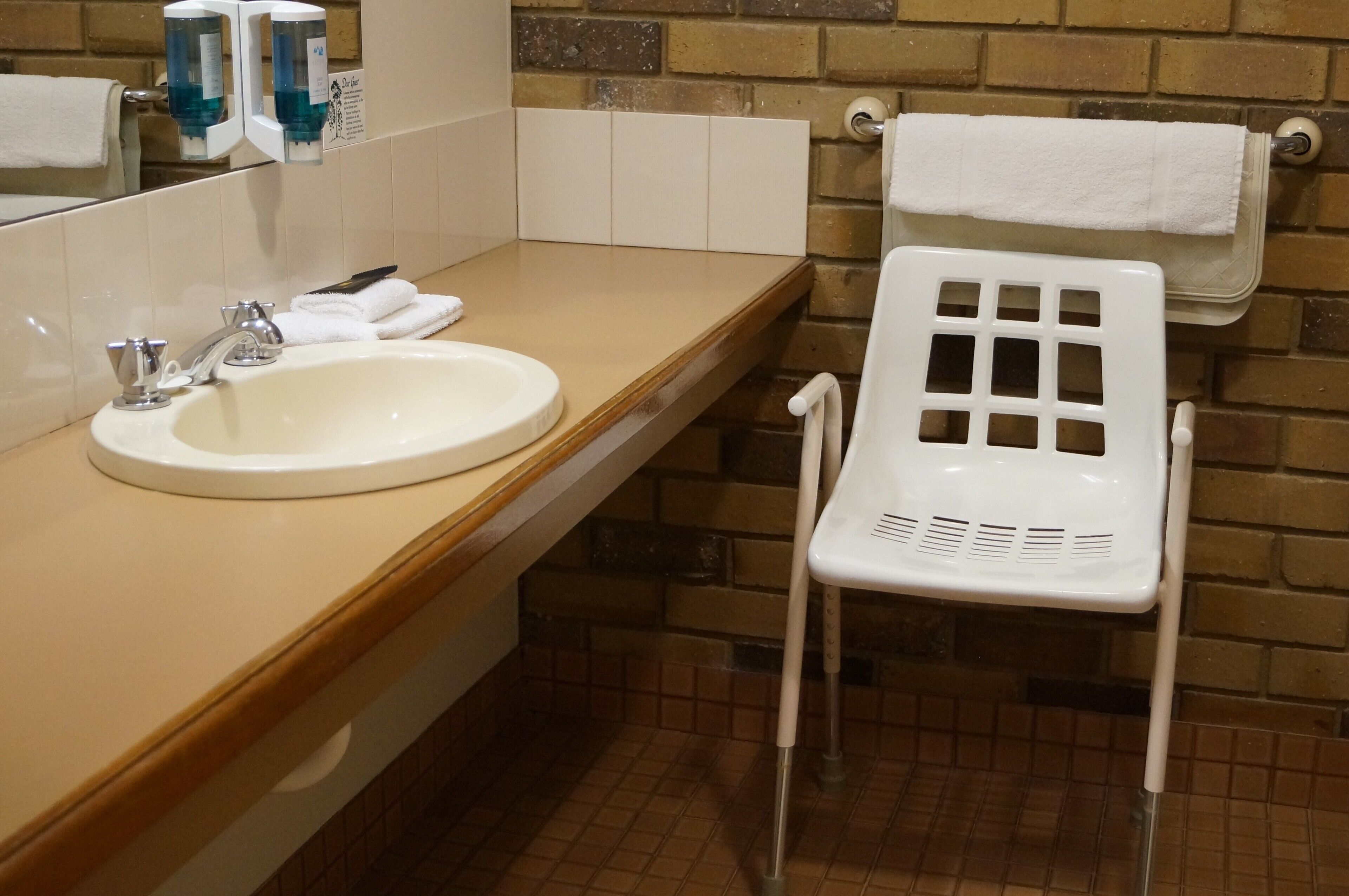 A bathroom with a sink, mirror, and a white plastic chair.