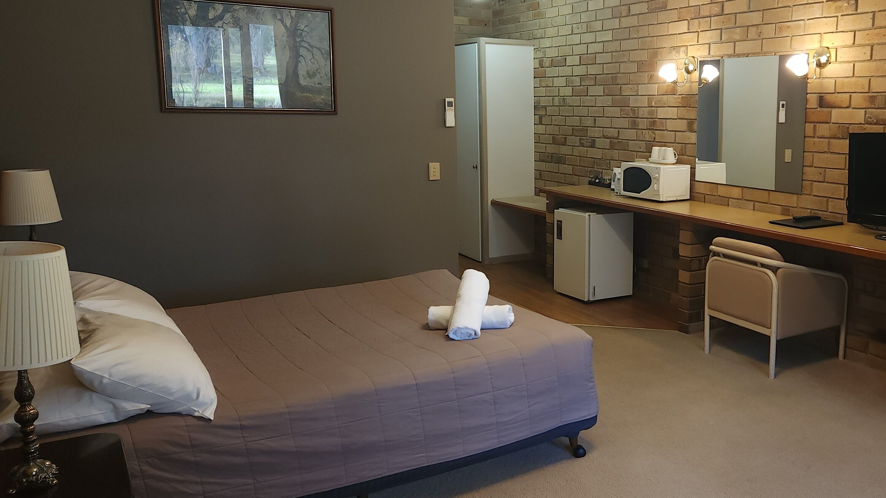 Una habitación de hotel con una cama, un escritorio con computadora, un refrigerador y un microondas.